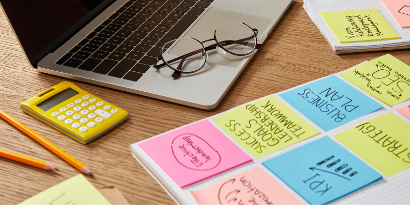 SEO goals on colored sticky notes with eyeglasses, laptop, and calculator on a wooden table.